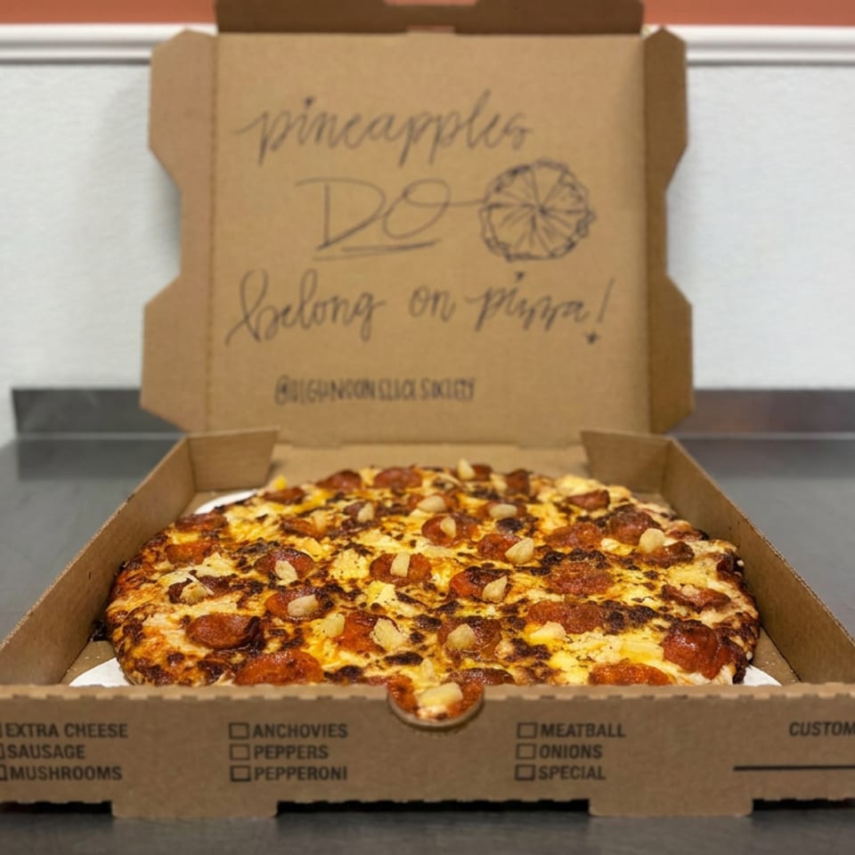 Square pizza topped with cheese, pepperoni, mushrooms, and pine nuts sits in an open cardboard delivery box.